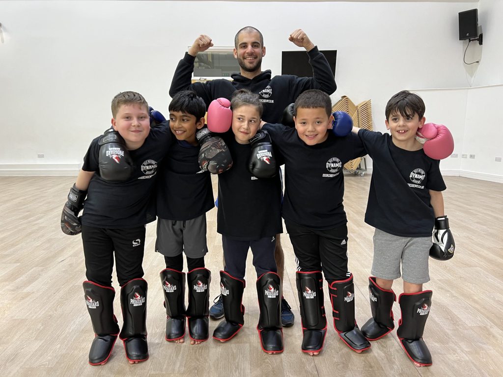 A group of children and trainer wearing boxing gloves, with their arms raised around each others' shoulders.