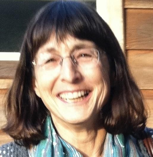 Head and shoulders of Judith Devons, a White female-presenting person who is smiling. Judith has shoulder-length dark hair and glasses.